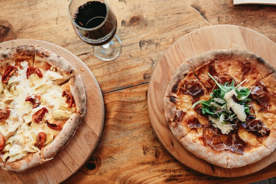 Duas pizzas acompanhadas por uma taça de vinho tinto para ilustrar harmonização