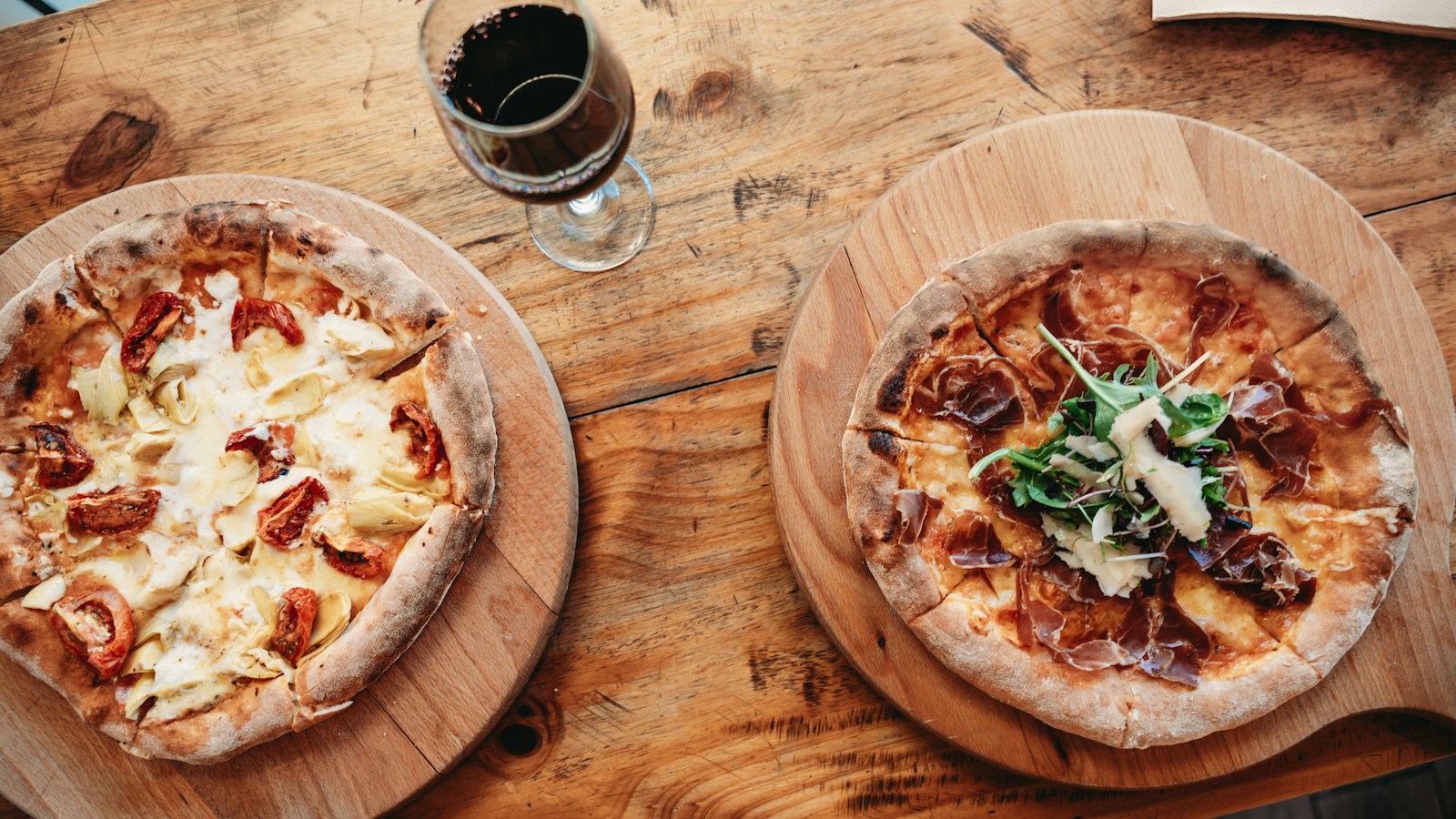 Duas pizzas acompanhadas por uma taça de vinho tinto para ilustrar harmonização